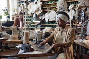 Sarto africano seduto sul suo posto di lavoro con macchina da cucire e prodotti da cucire in fabbrica
