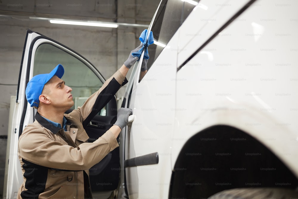 Professional auto service worker wiping car surface with microfiber cloth, horizontal medium shot, copy space