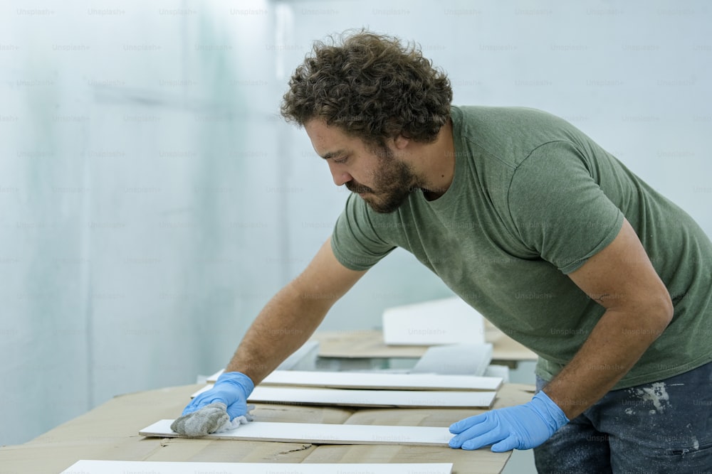 Un homme en chemise verte et gants bleus travaillant sur un morceau de papier
