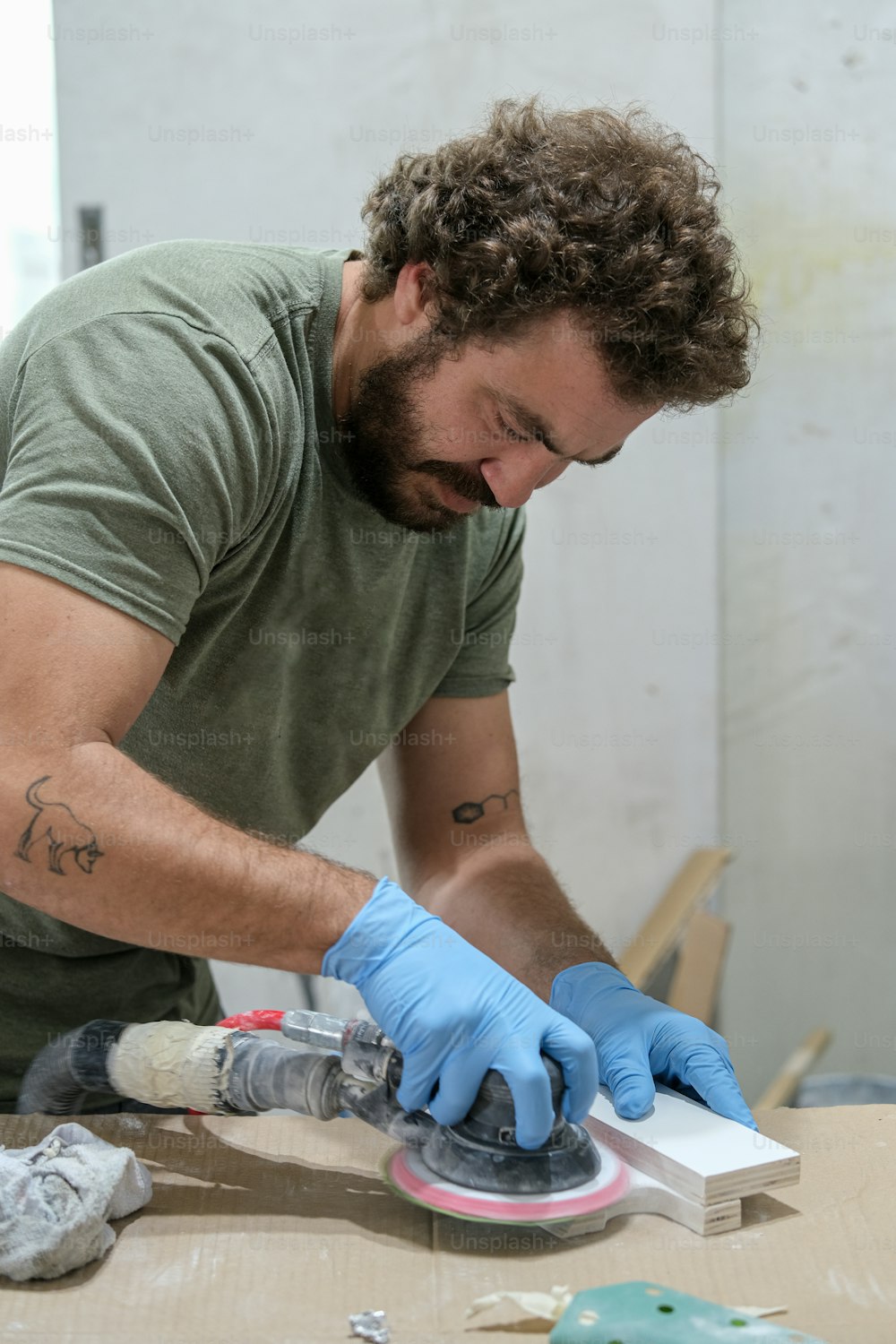 a man in a green shirt and blue gloves sanding a piece of paper