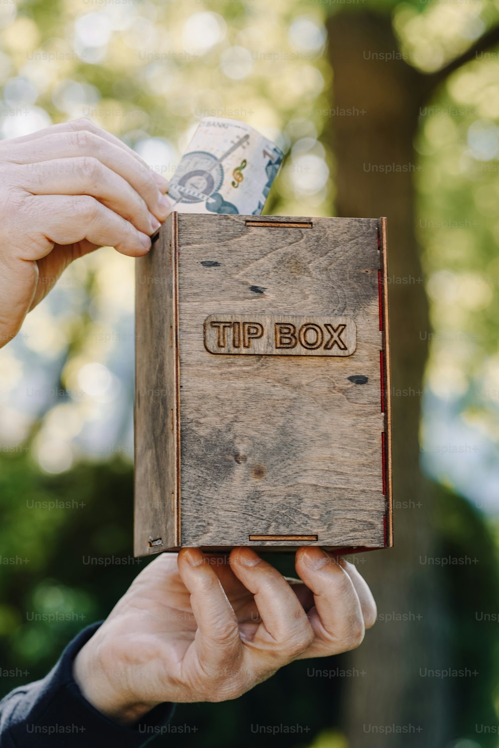a person holding a wooden box with a stack of money in it
