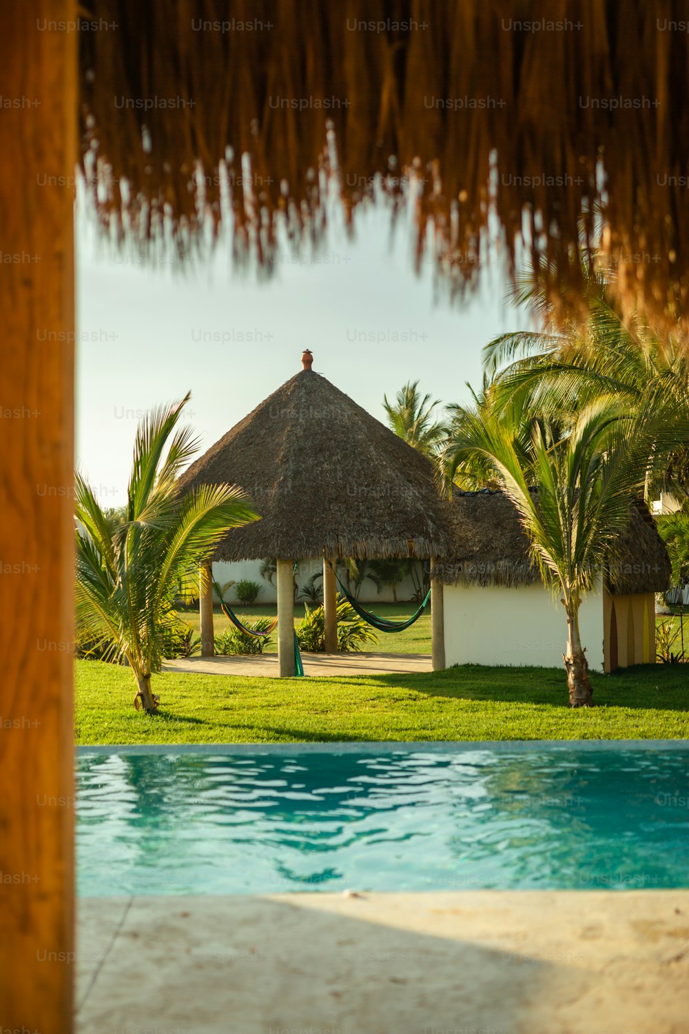uma piscina com um telhado de colmo e palmeiras