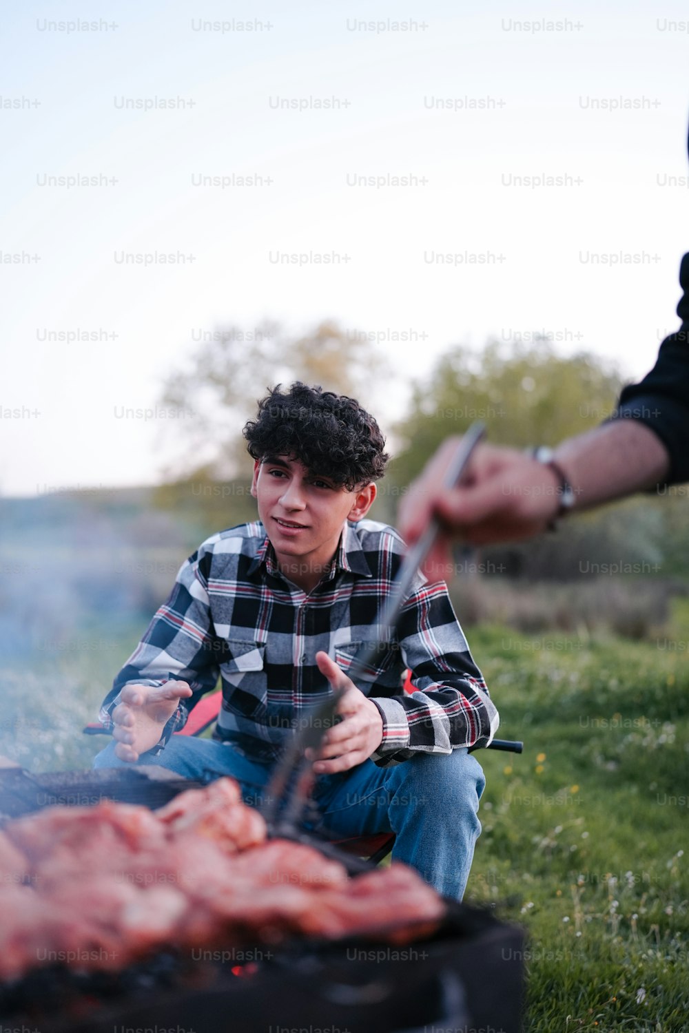 a man sitting in front of a grill with meat on it
