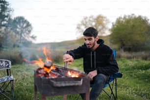um homem sentado em uma cadeira ao lado de uma fogueira