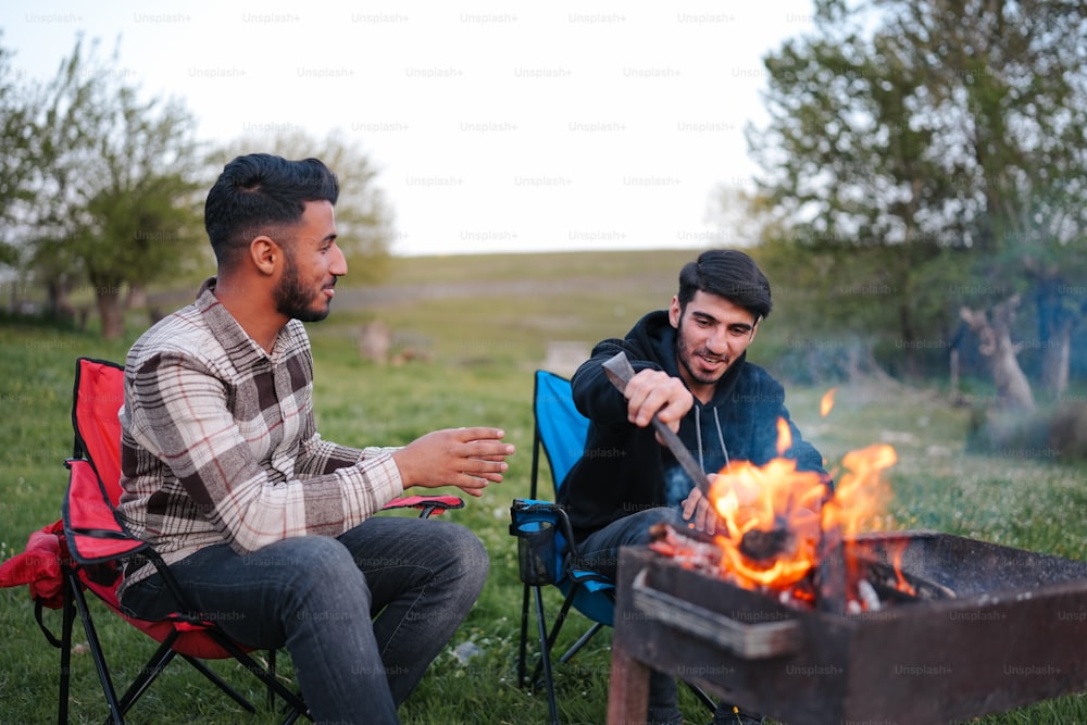 a couple of men sitting next to a fire pit