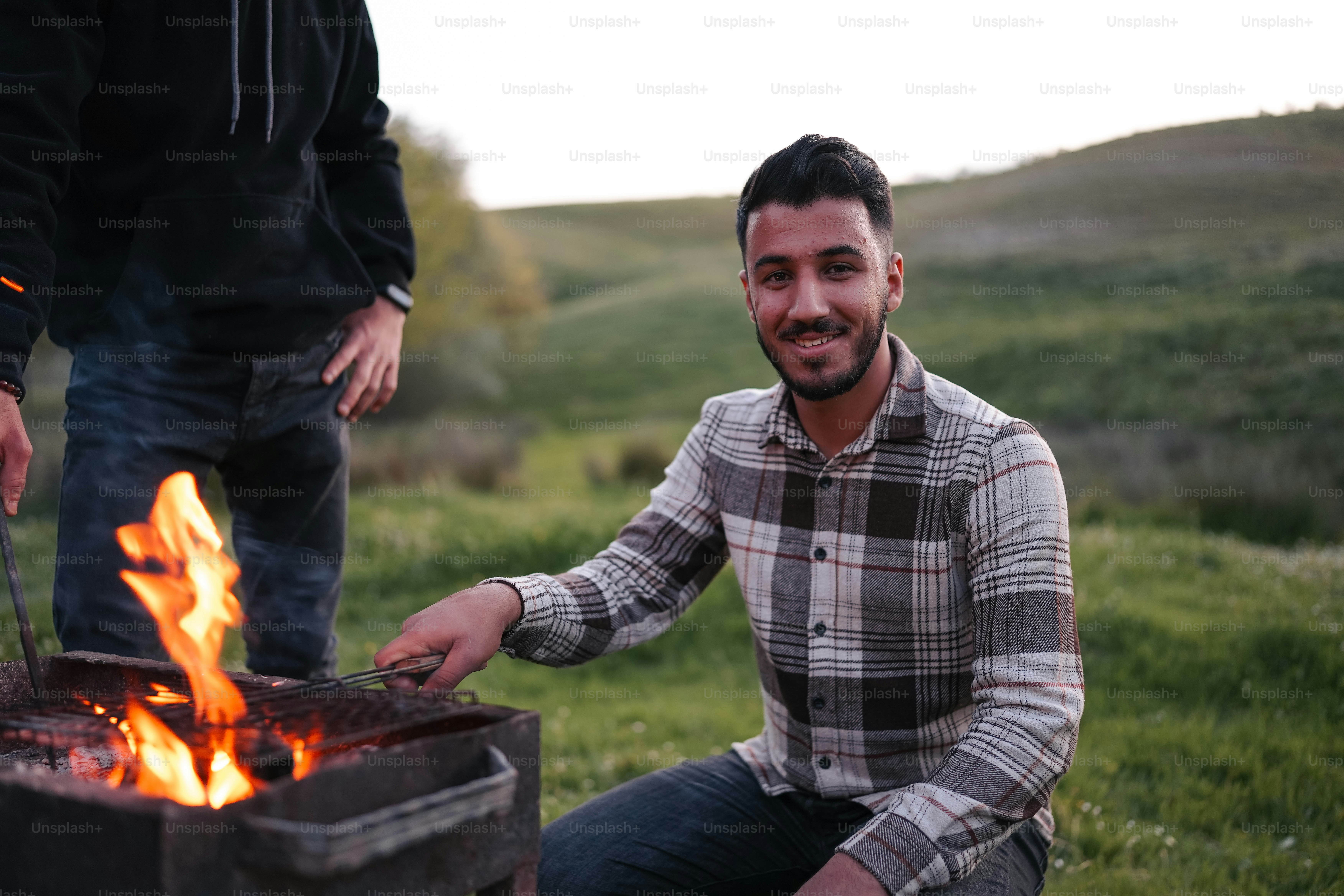 a man sitting next to a fire in a field