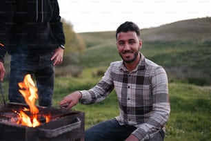 a man sitting next to a fire in a field