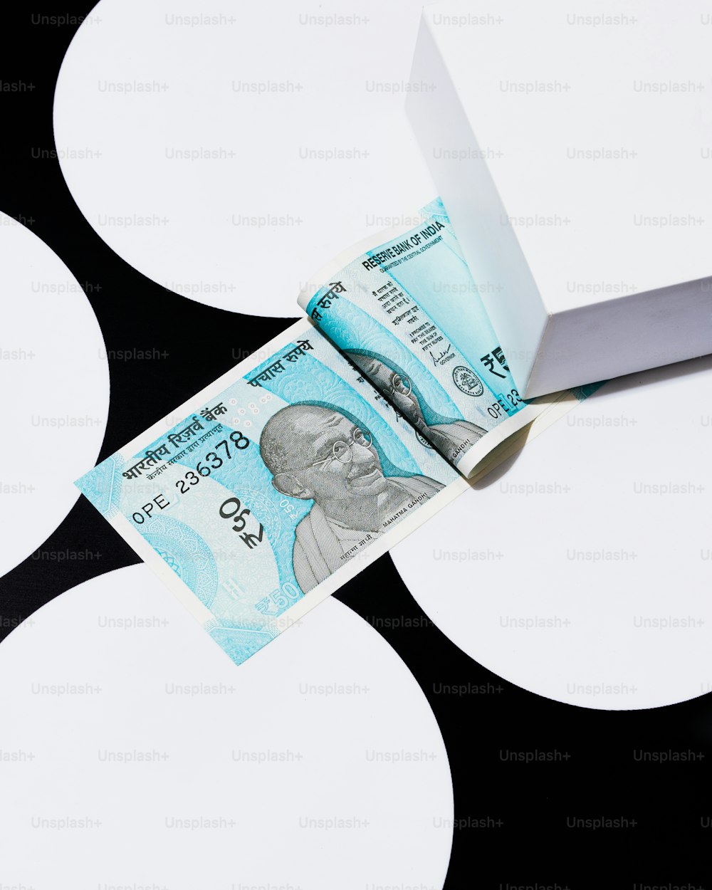Un billete indio de cinco rupias sobresaliendo de un pedazo de papel
