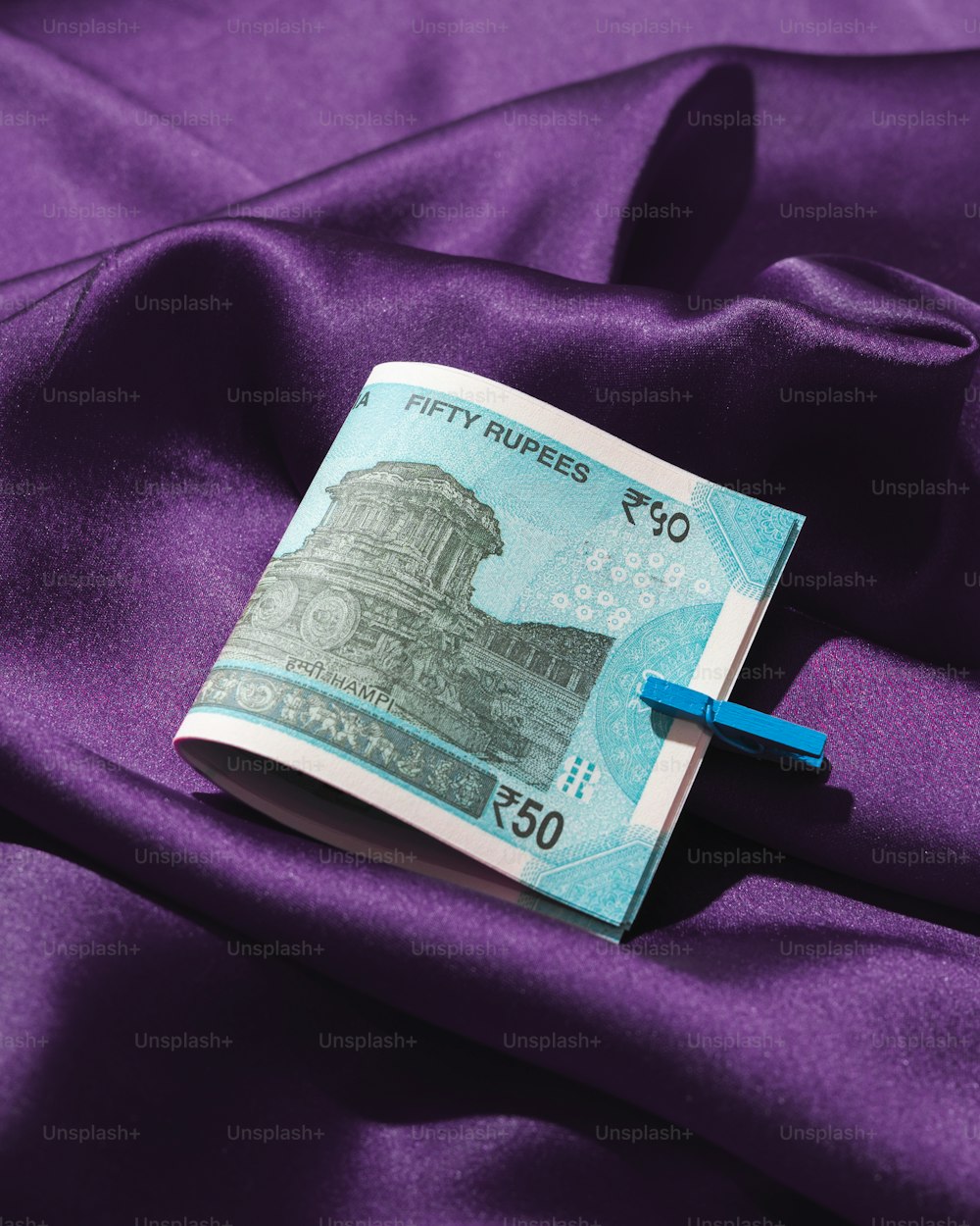 a fifty rupees note laying on a purple satin