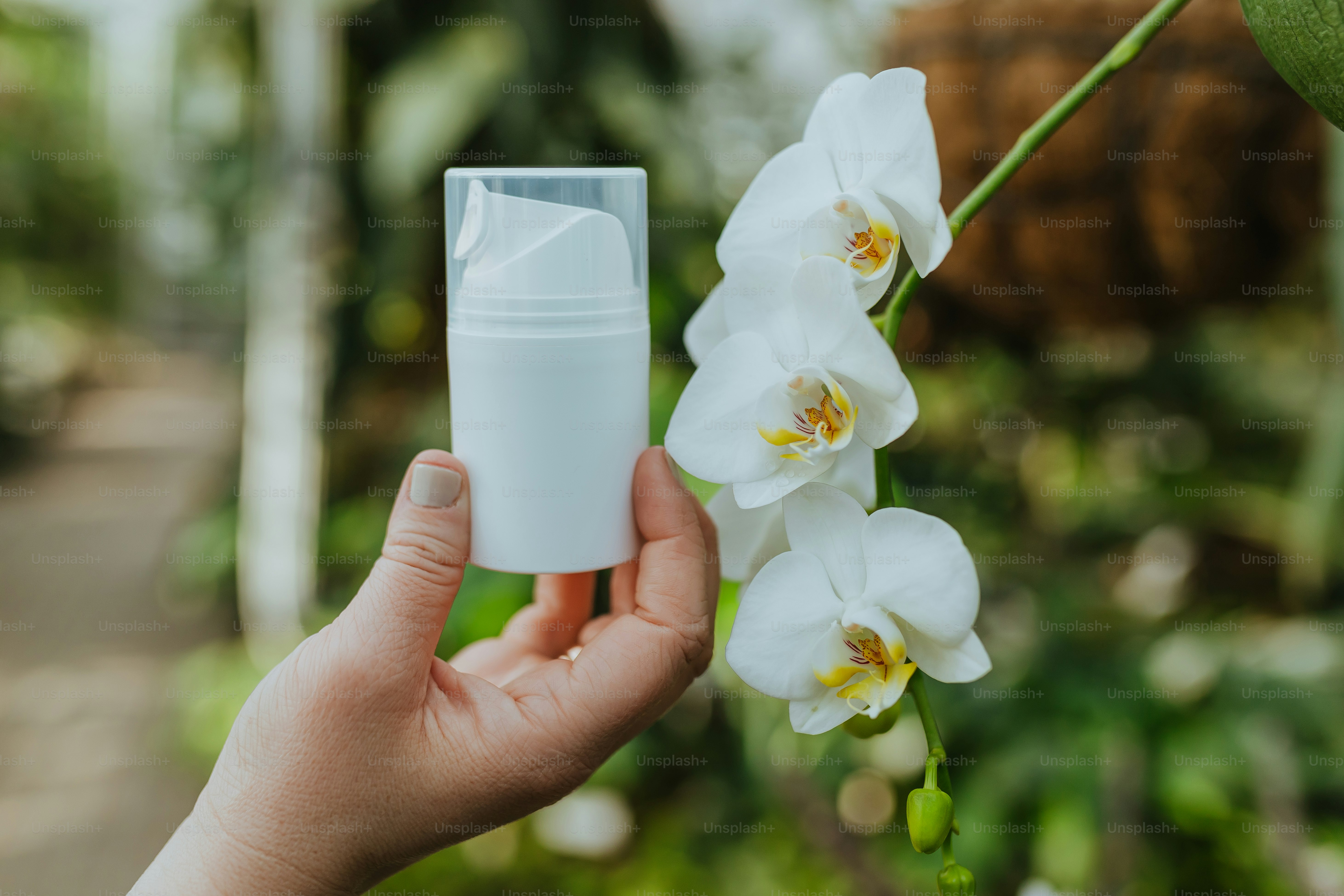 una mano che tiene una bottiglia bianca con un fiore bianco sullo sfondo