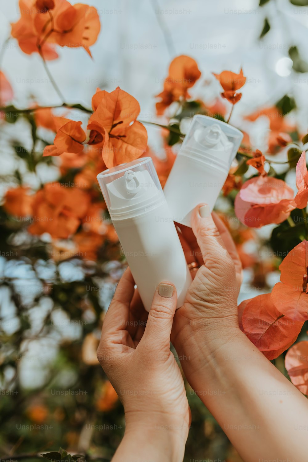 a person holding a tube of lotion in front of flowers