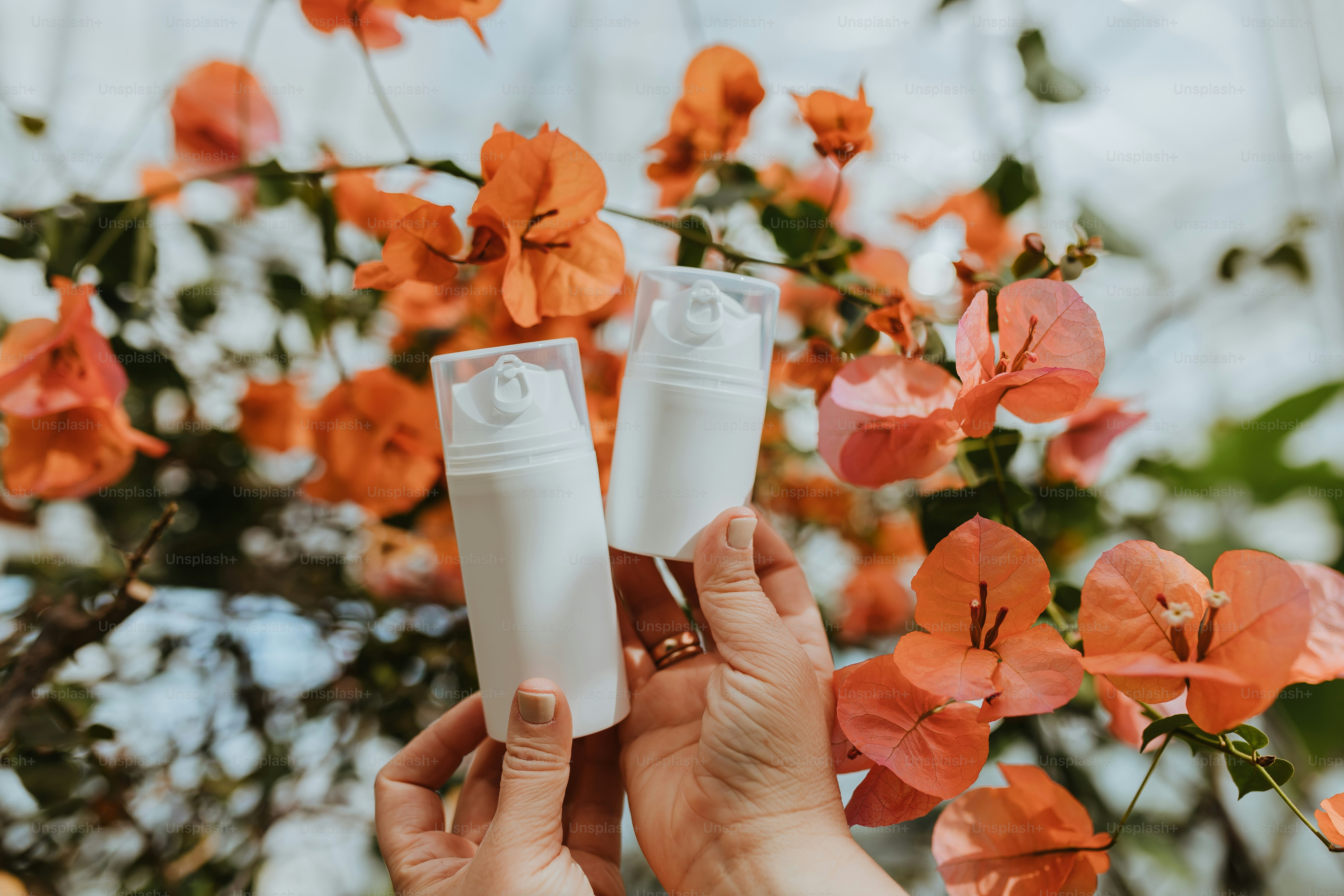 una persona che tiene due tubetti di lozione davanti ai fiori d'arancio