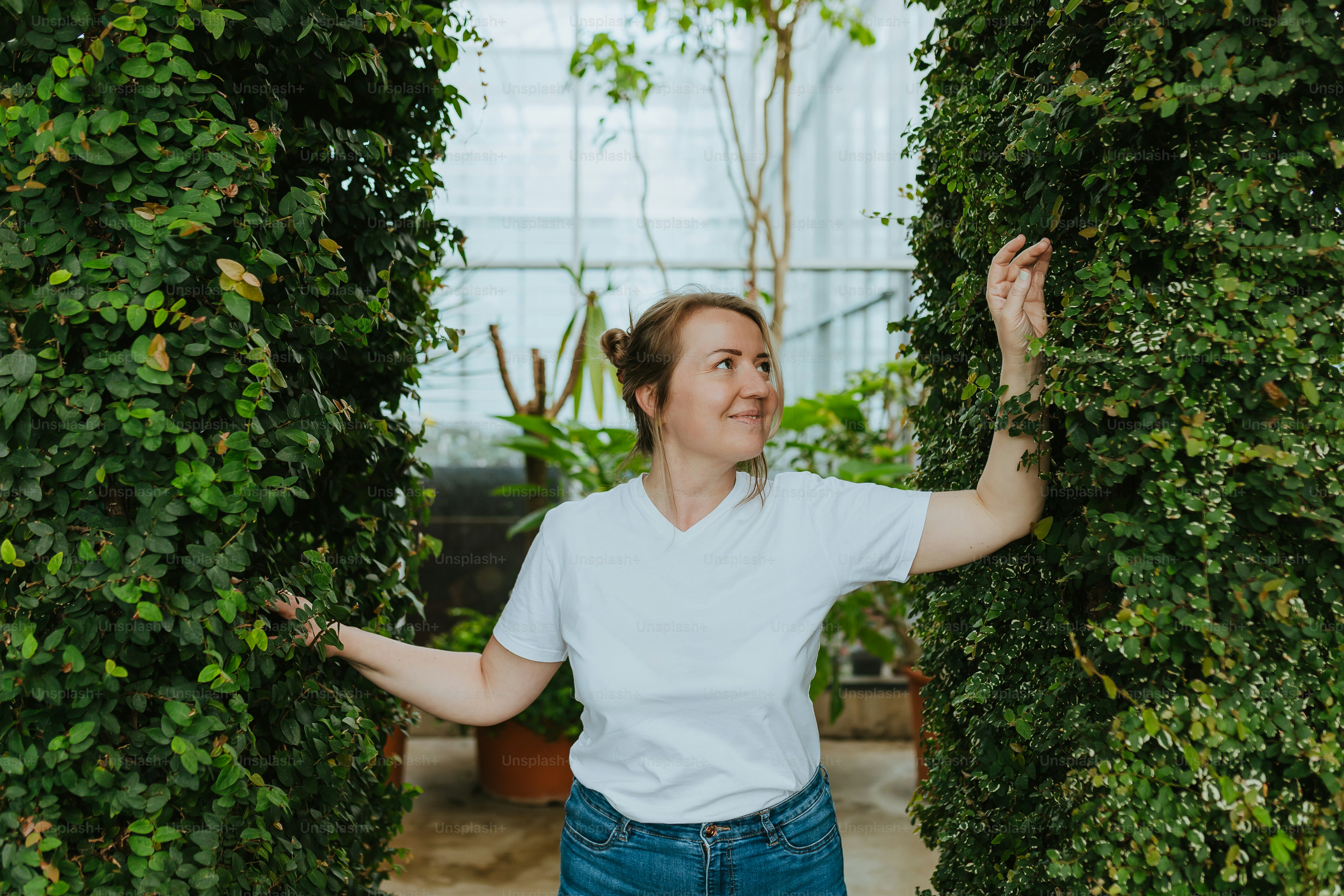 Una donna in una camicia bianca in piedi tra due cespugli verdi