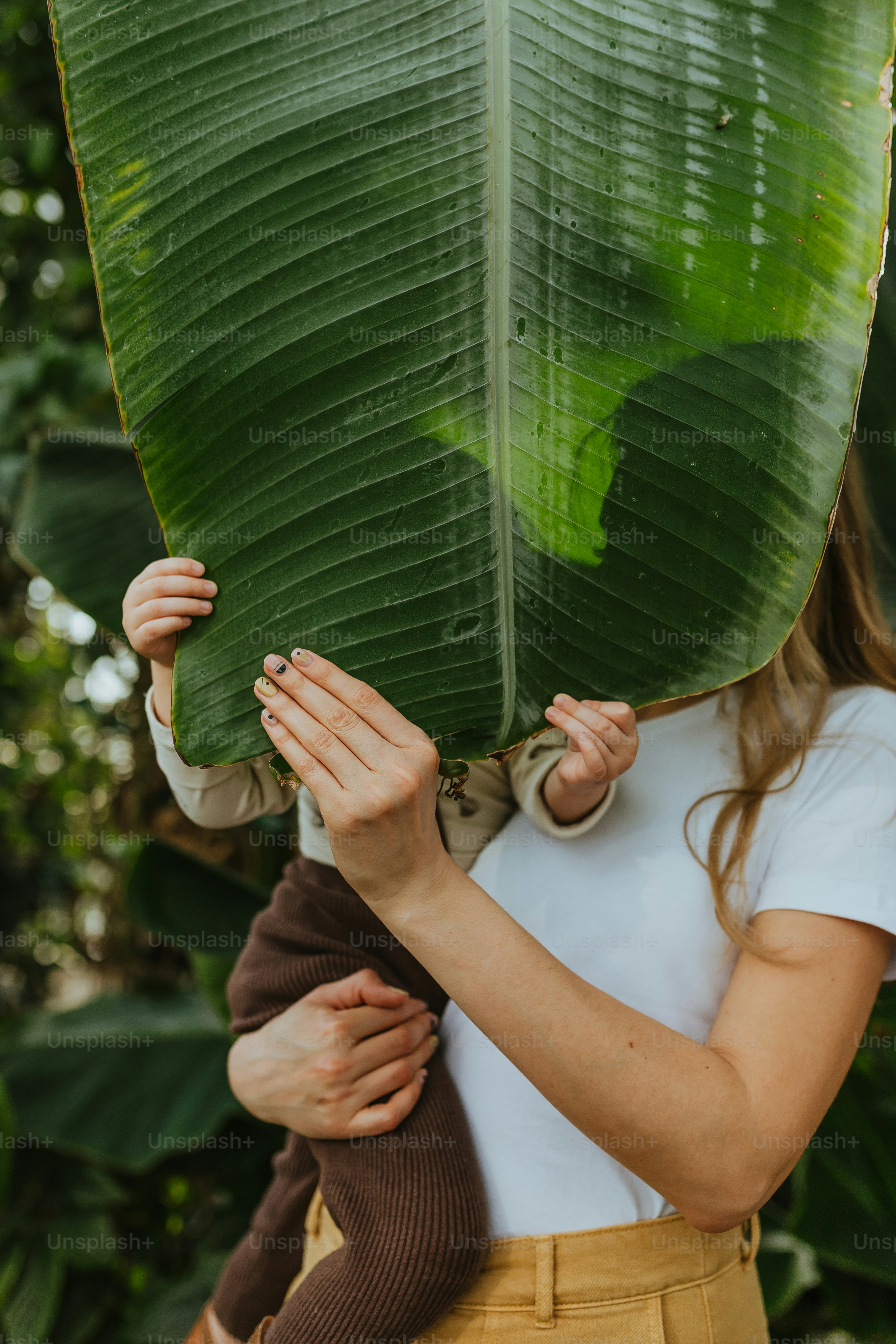 a woman holding a large green leaf over her face