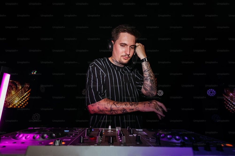 Un hombre con un brazo tatuado parado frente a un DJ set