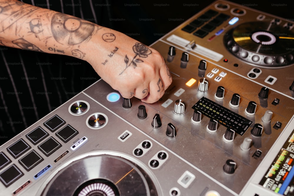 Un hombre con un tatuaje en el brazo tocando un mezclador de DJ