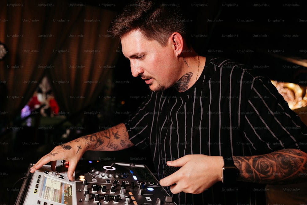 Un hombre con un tatuaje en el brazo está usando un controlador DJ