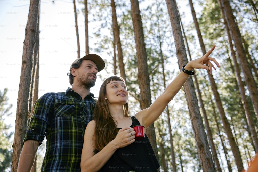 a man and a woman standing in a forest pointing at something