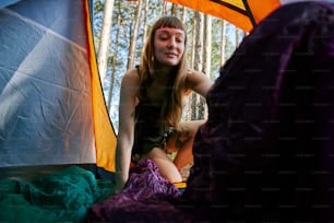a woman sitting inside of a tent next to a forest