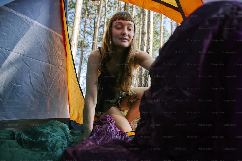 a woman sitting inside of a tent next to a forest