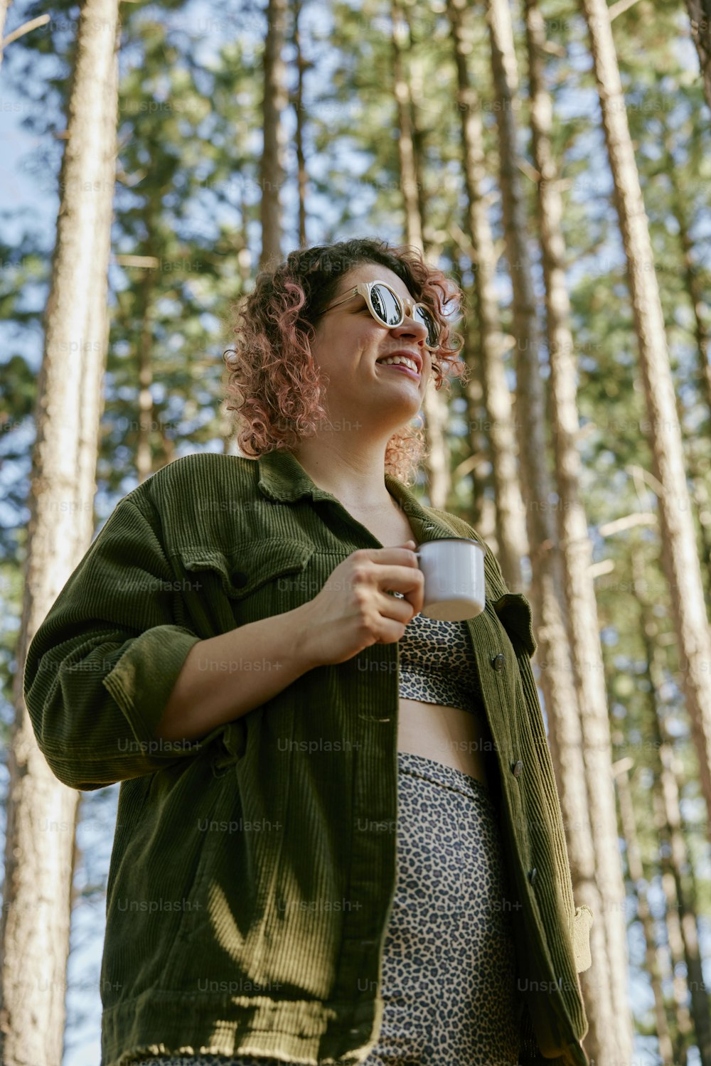 Una mujer parada en un bosque sosteniendo una taza de café