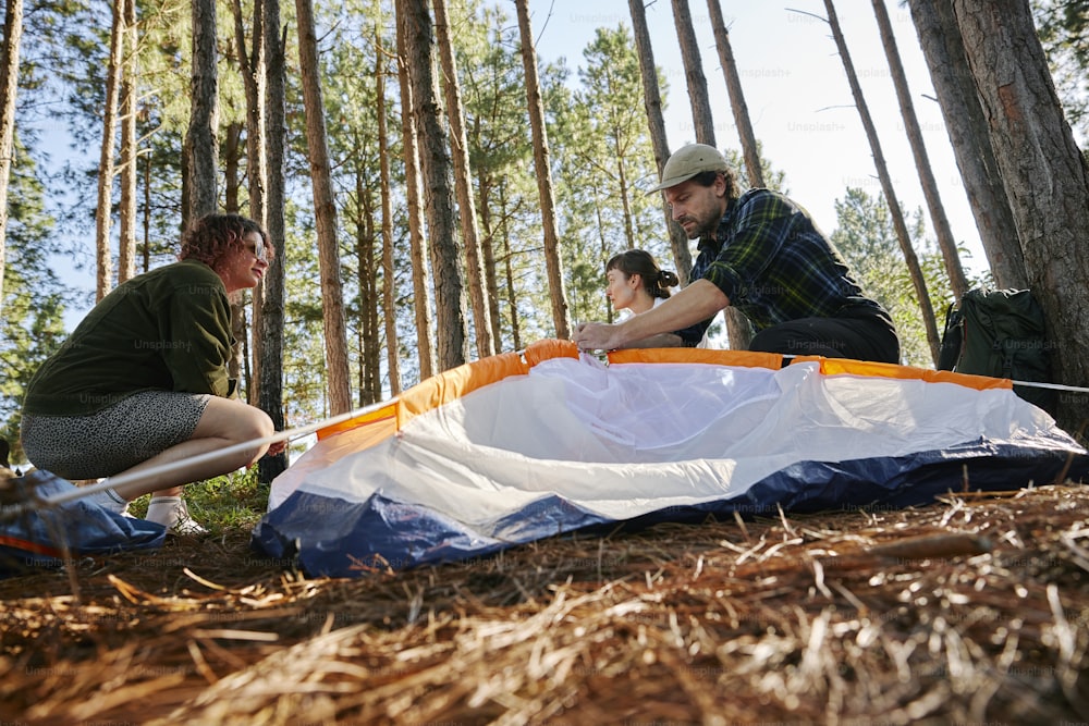 a man and a woman setting up a tent in the woods