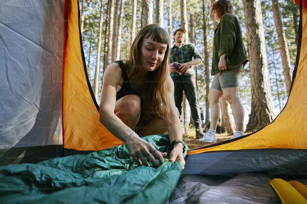 a woman is setting up a tent in the woods