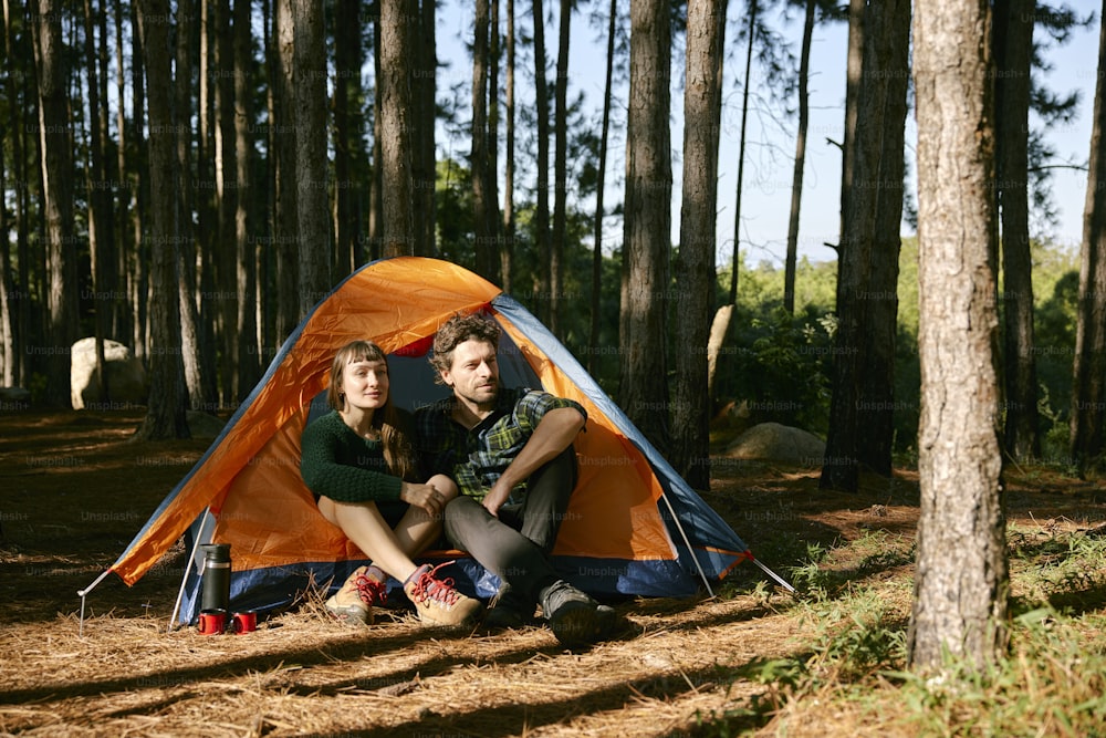 um homem e uma mulher sentados em uma tenda na floresta