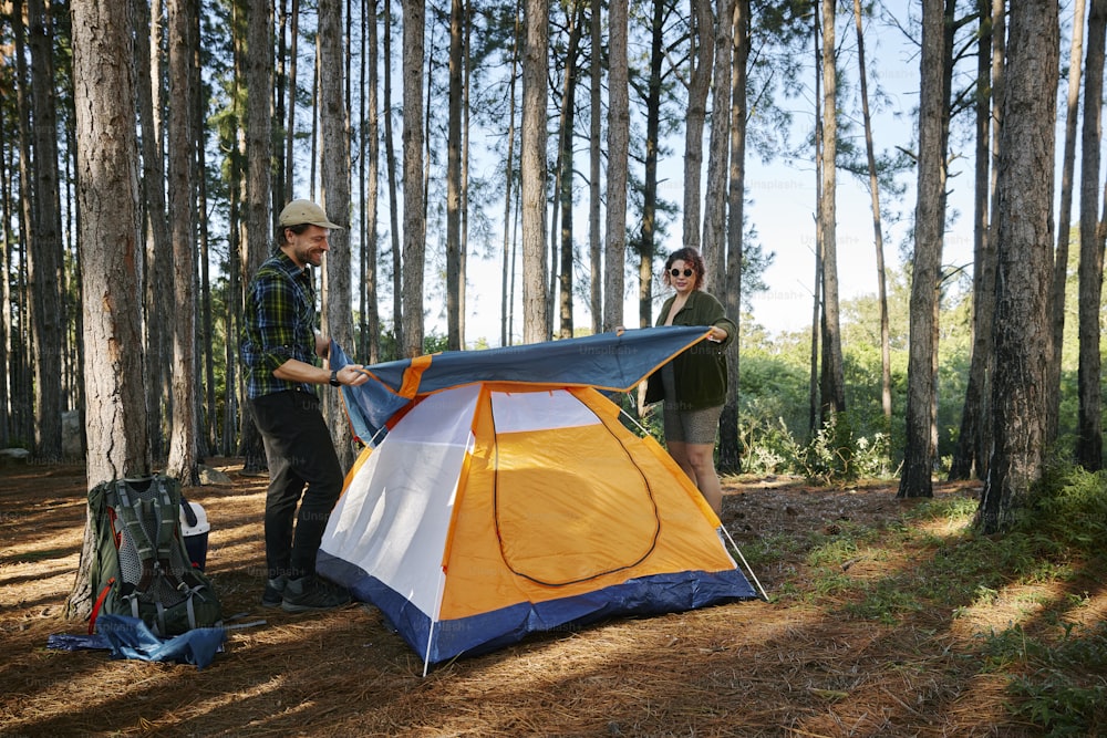 dois homens de pé ao lado de uma tenda na floresta