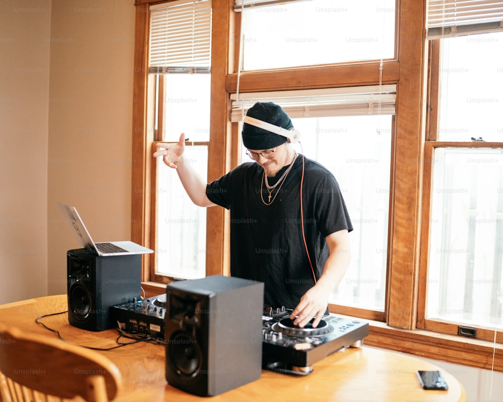a man standing at a table with a laptop and dj equipment