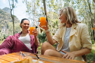 a couple of women sitting next to each other holding glasses of orange juice