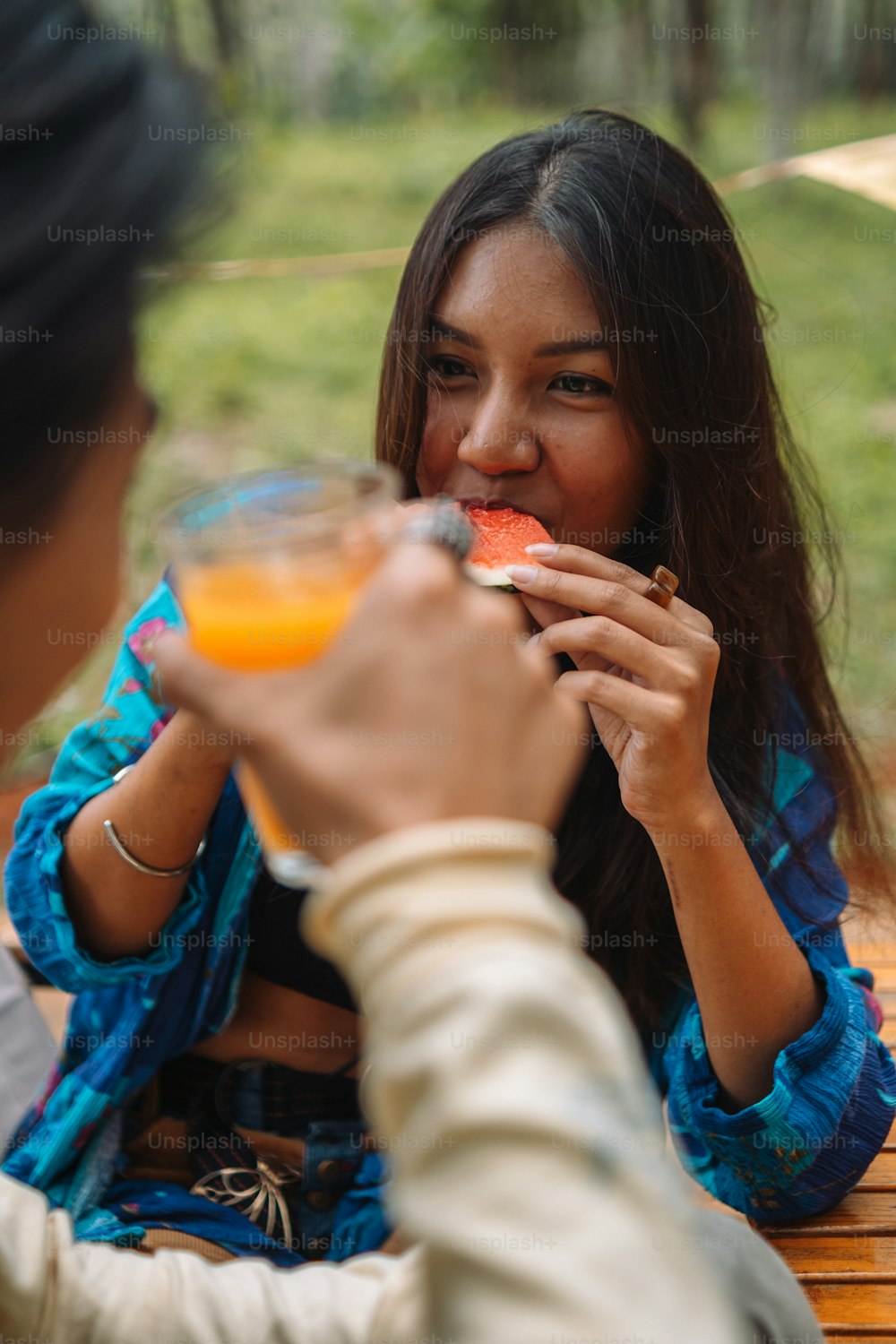 a woman eating a piece of watermelon and drinking a glass of orange juice