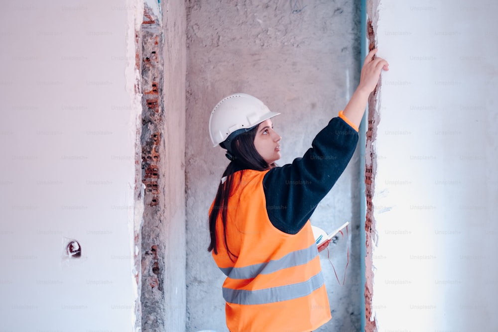 a woman in a hard hat and safety vest working on a wall