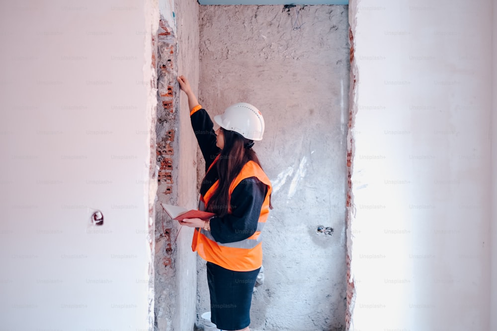 a woman in a hard hat and safety vest working on a wall