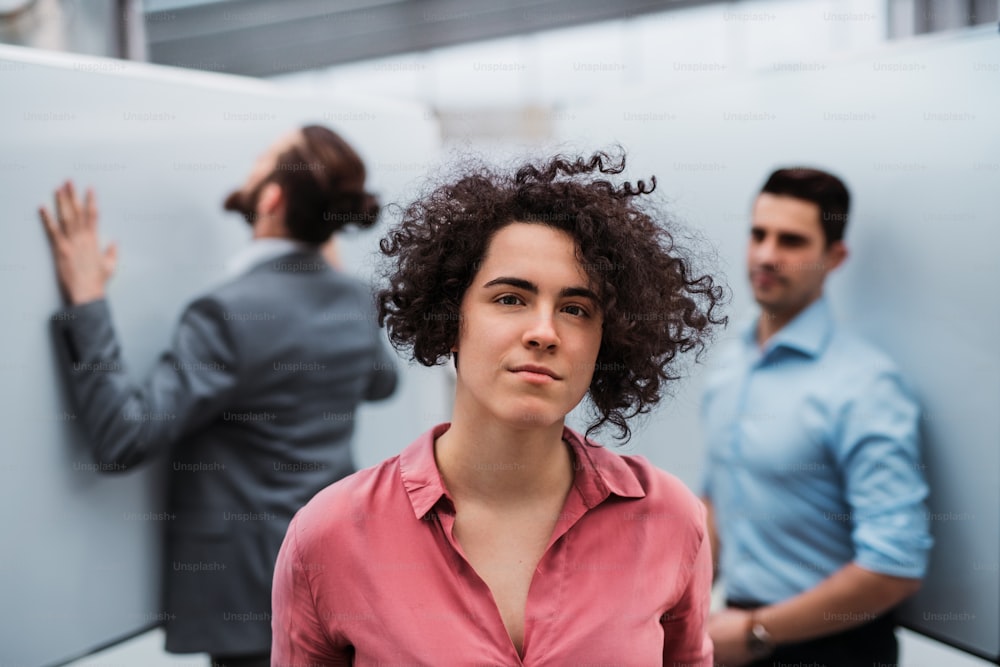 A portrait of young businesswoman standing in office, colleagues in the background.