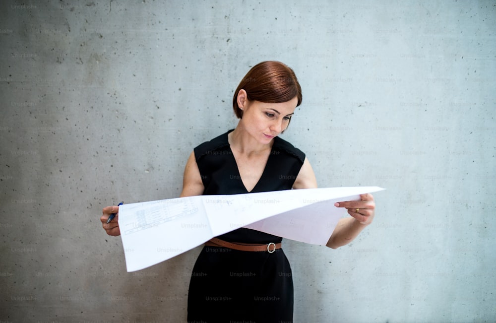 Eine junge Geschäftsfrau oder Architektin, die im Büro steht und sich Blaupausen ansieht.