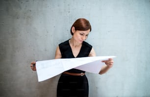 A young businesswoman or architect standing in office, looking at blueprints.