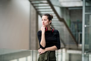 A portrait of happy young businesswoman with headphones standing in corridor outside office.