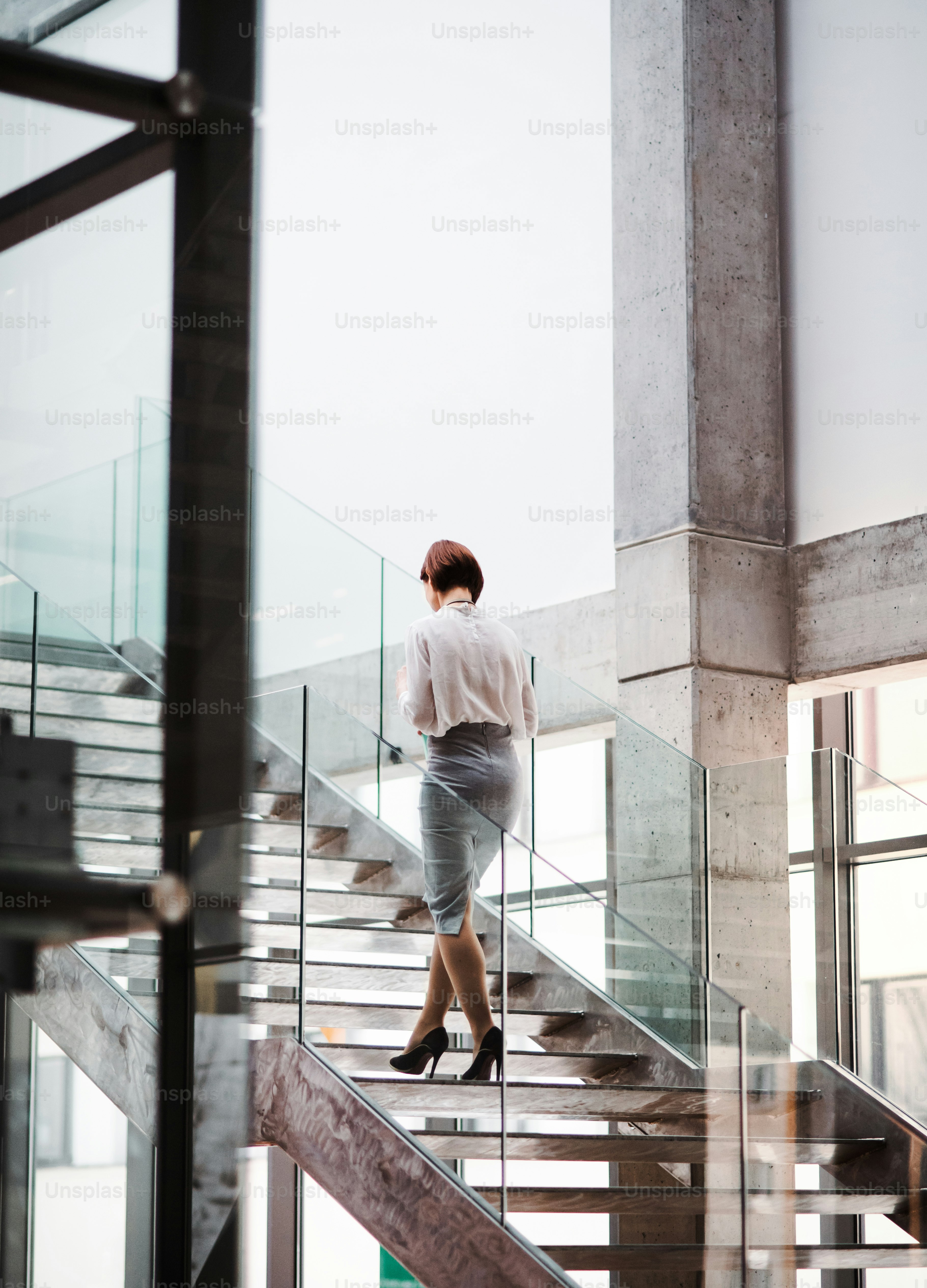 Una vista trasera de una joven empresaria subiendo las escaleras en el edificio de oficinas. Espacio de copia.