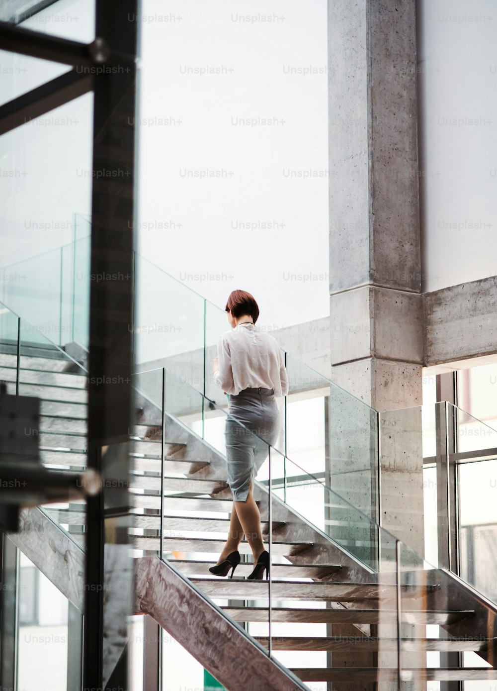 Eine Rückansicht einer jungen Geschäftsfrau, die die Treppe im Bürogebäude hinaufgeht. Speicherplatz kopieren.