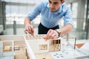 Young businessman or architect with model of a house standing at the desk in office, working.