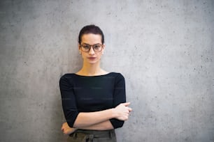 A portrait of young businesswoman with glasses standing in office, looking at camera.
