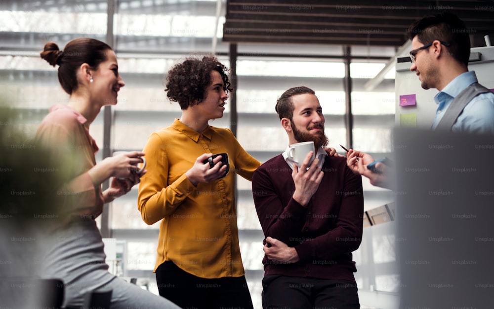 Eine Gruppe fröhlicher junger Geschäftsleute mit einer Tasse Kaffee steht im Büro und unterhält.