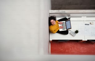 A top view of young businesswoman or architect sitting on desk in an office, using laptop. Copy space.