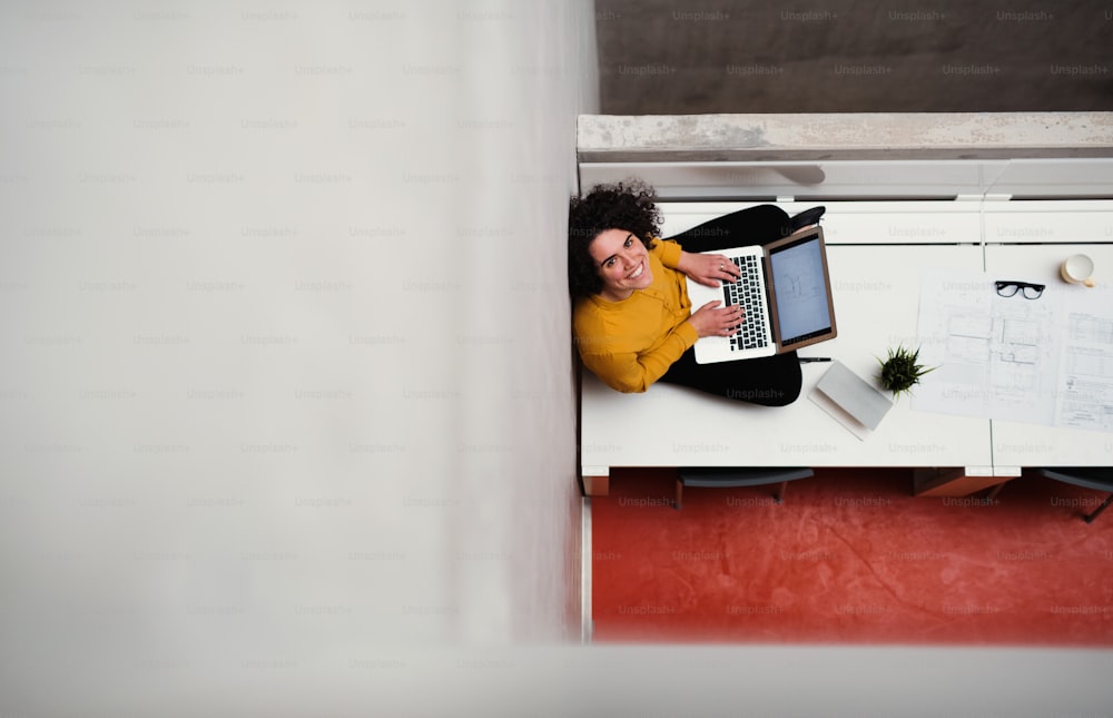 A top view of young businesswoman or architect sitting on desk in an office, using laptop. Copy space.