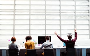 A rear view of group of young businesspeople with computers and VR goggles working in office. Copy space.