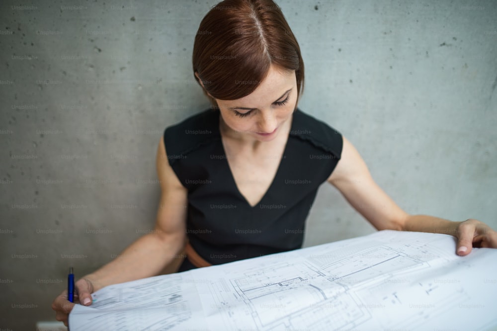 Una joven empresaria o arquitecta parada en la oficina, mirando planos.