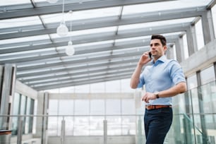 Una vista de bajo ángulo de un joven hombre de negocios serio con un teléfono inteligente en el pasillo fuera de la oficina, haciendo una llamada telefónica.