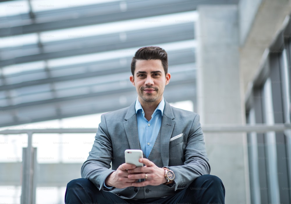 Um retrato de um jovem empresário feliz com smartphone sentado no corredor do lado de fora do escritório.
