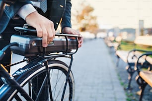 Una sección media de viajeros de negocios que instala una bicicleta eléctrica cuando viaja a casa desde el trabajo en la ciudad.